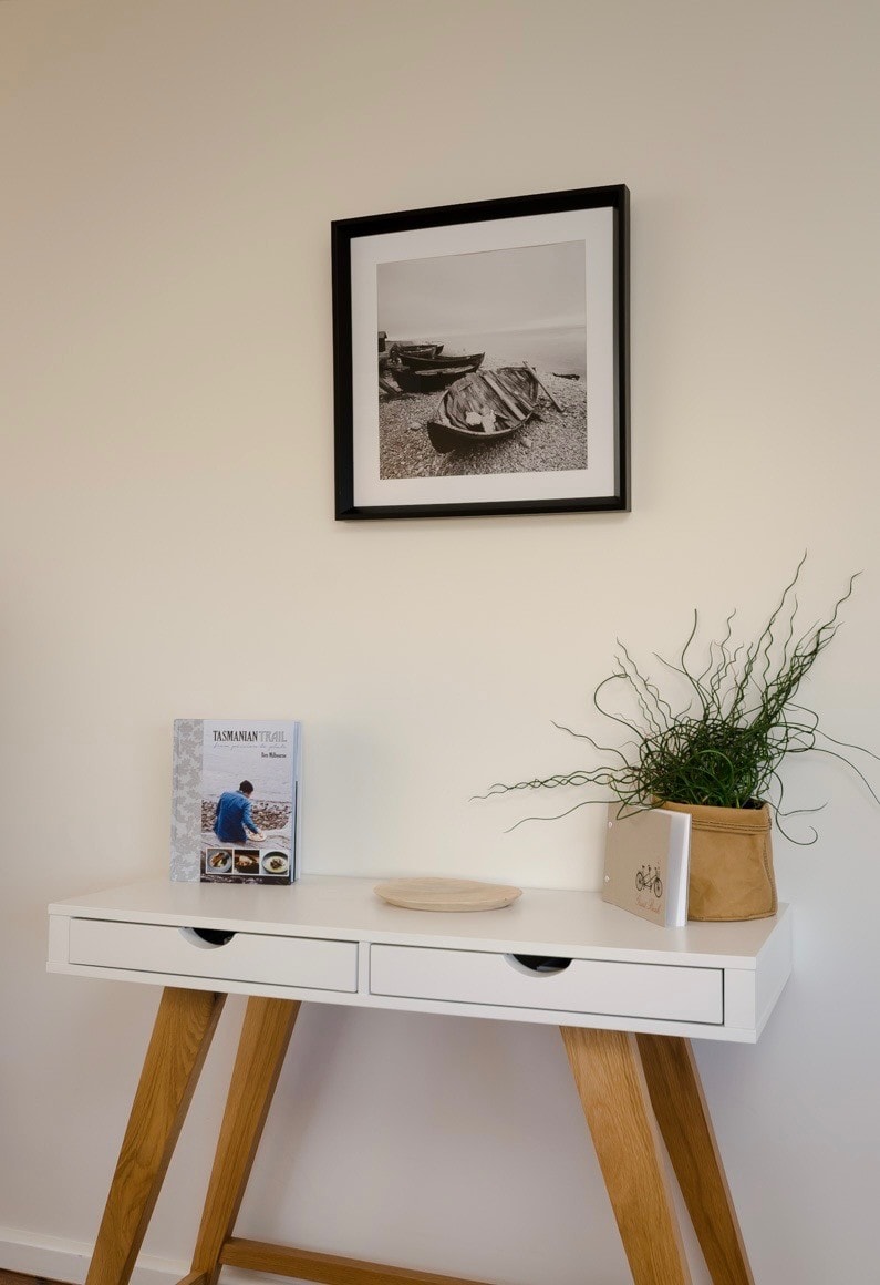 White console table with Tasmanian Trail book, coastal plant and framed boat artwork