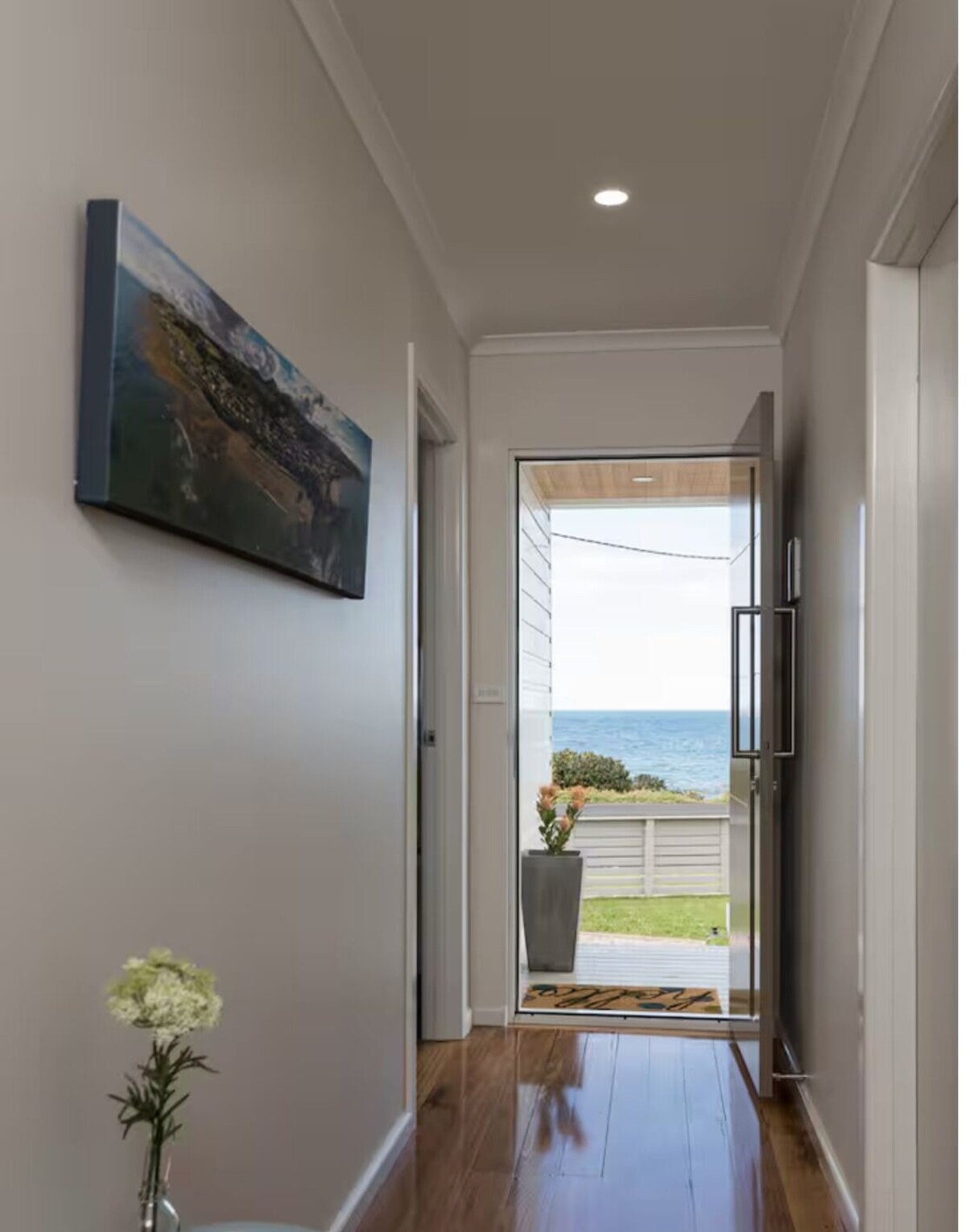Hallway with polished timber floors, coastal artwork and ocean views through the front door