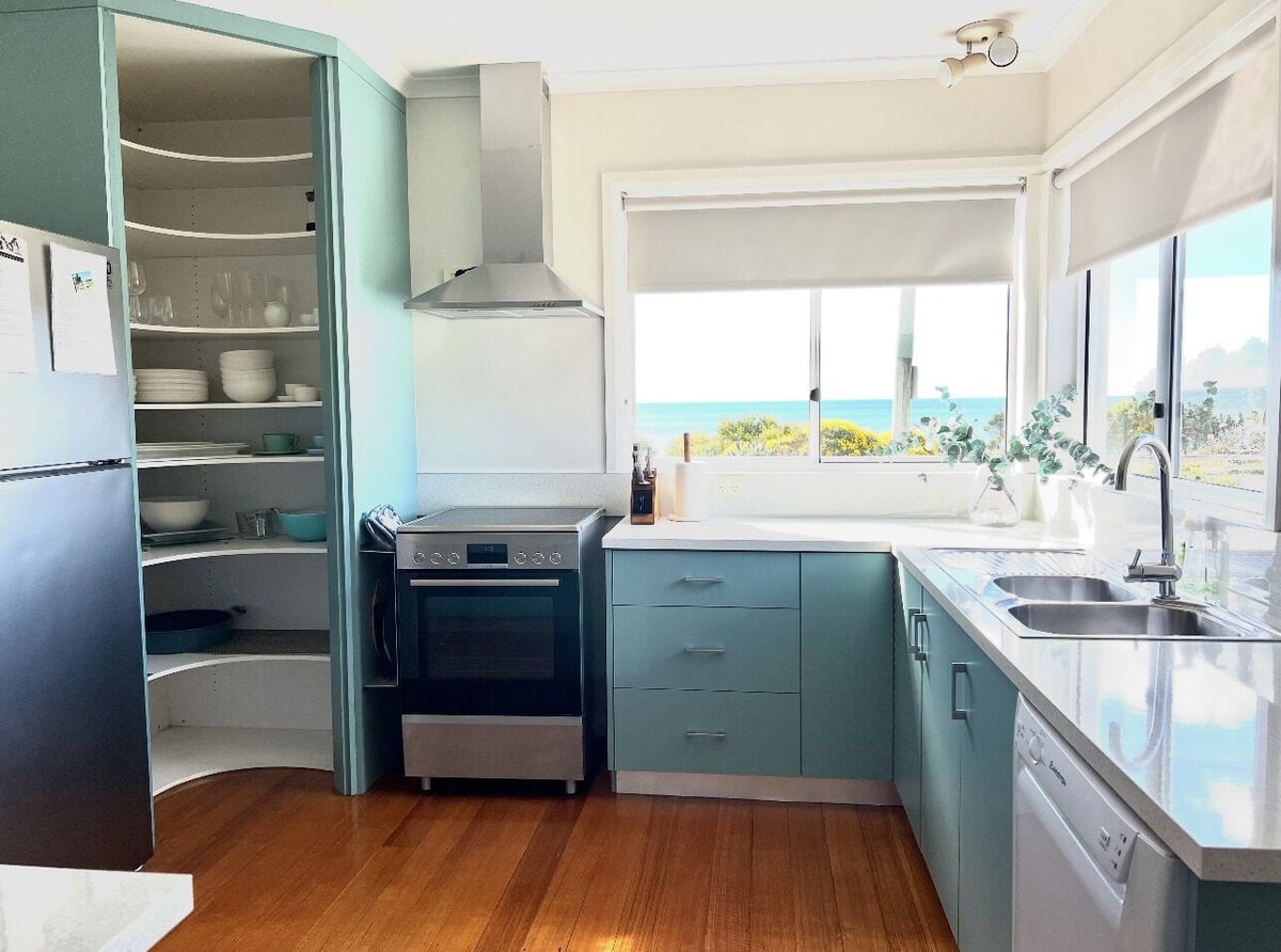 Teal kitchen with curved pantry, stainless oven and ocean views through the window
