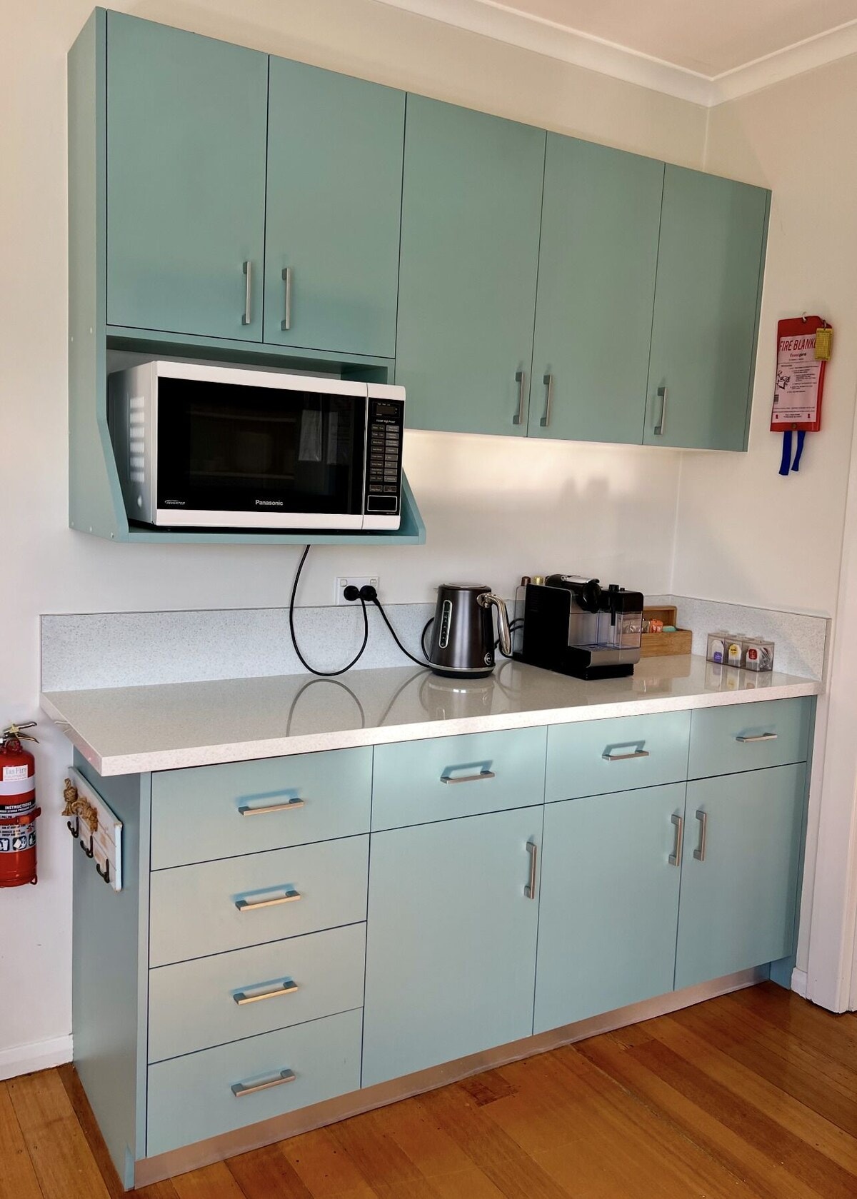 Teal kitchen cabinets with stone benchtop, microwave, kettle and Nespresso machine
