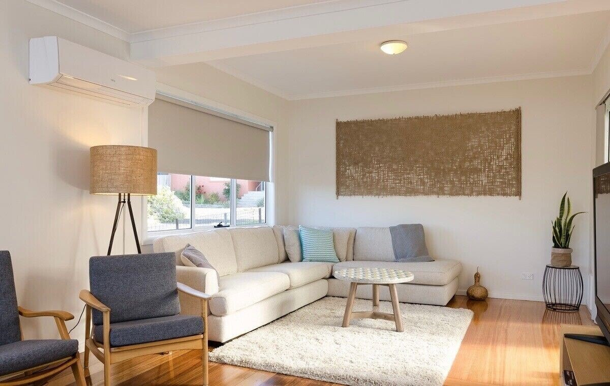 Bright lounge room with sectional sofa, armchair, floor lamp and coastal wall art
