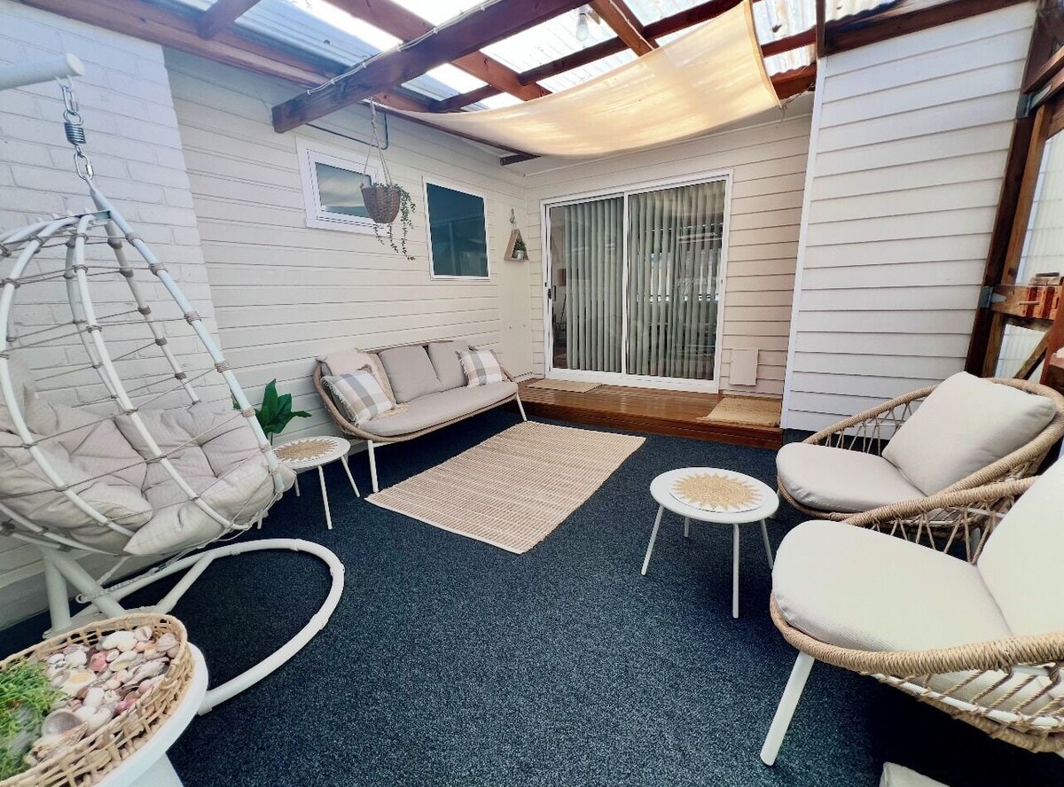 Sunroom with hanging egg chair, rattan sofa and armchairs under a sail shade