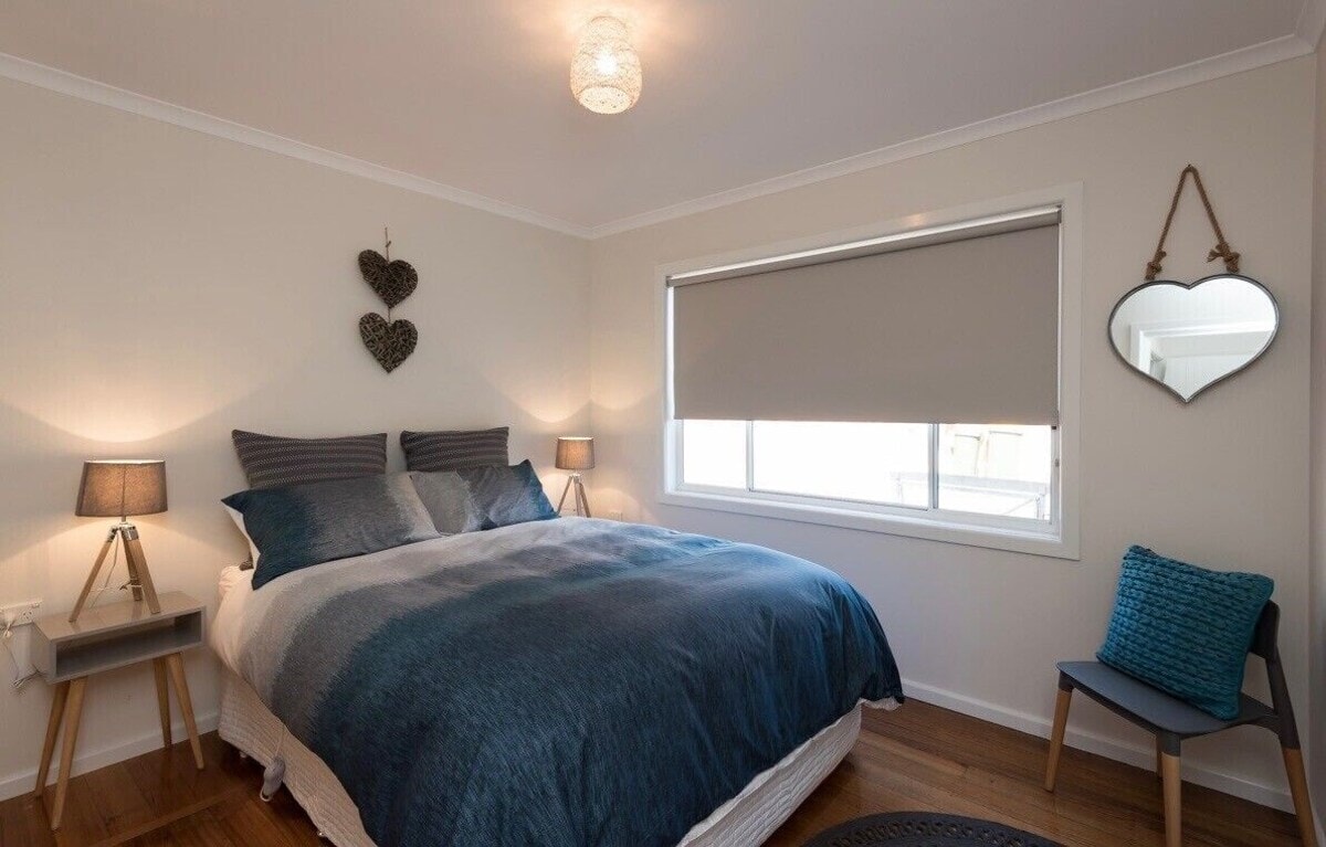 Cosy bedroom with blue linen, timber floors, bedside lamps and heart wall decor at Penguin Beach House