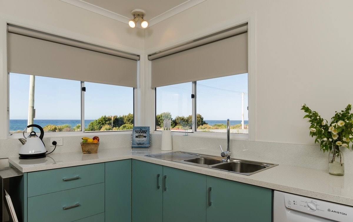 Kitchen with seafoam cabinetry, double sink and stunning ocean views through corner windows at Penguin Beach House