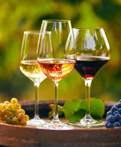 Three glasses of white, rosé and red wine on a barrel with fresh grapes